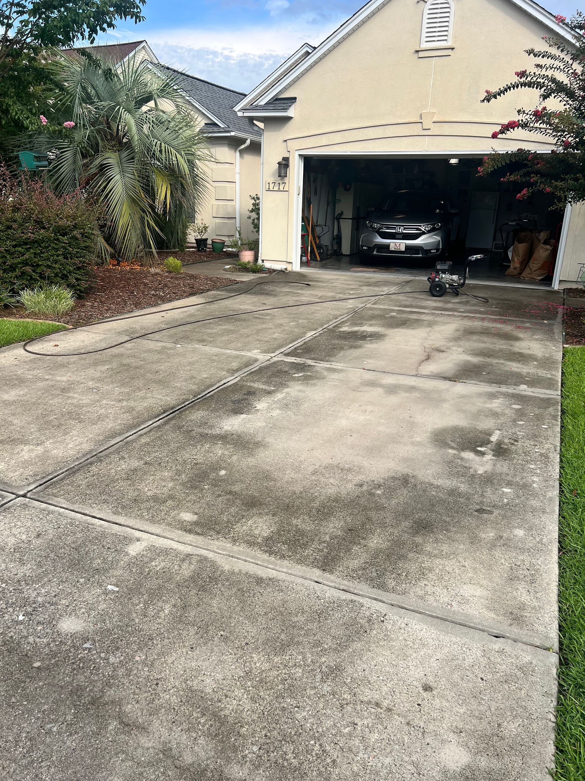 Driveway in front of a house with a car parked in the garage; gray concrete with discoloration.