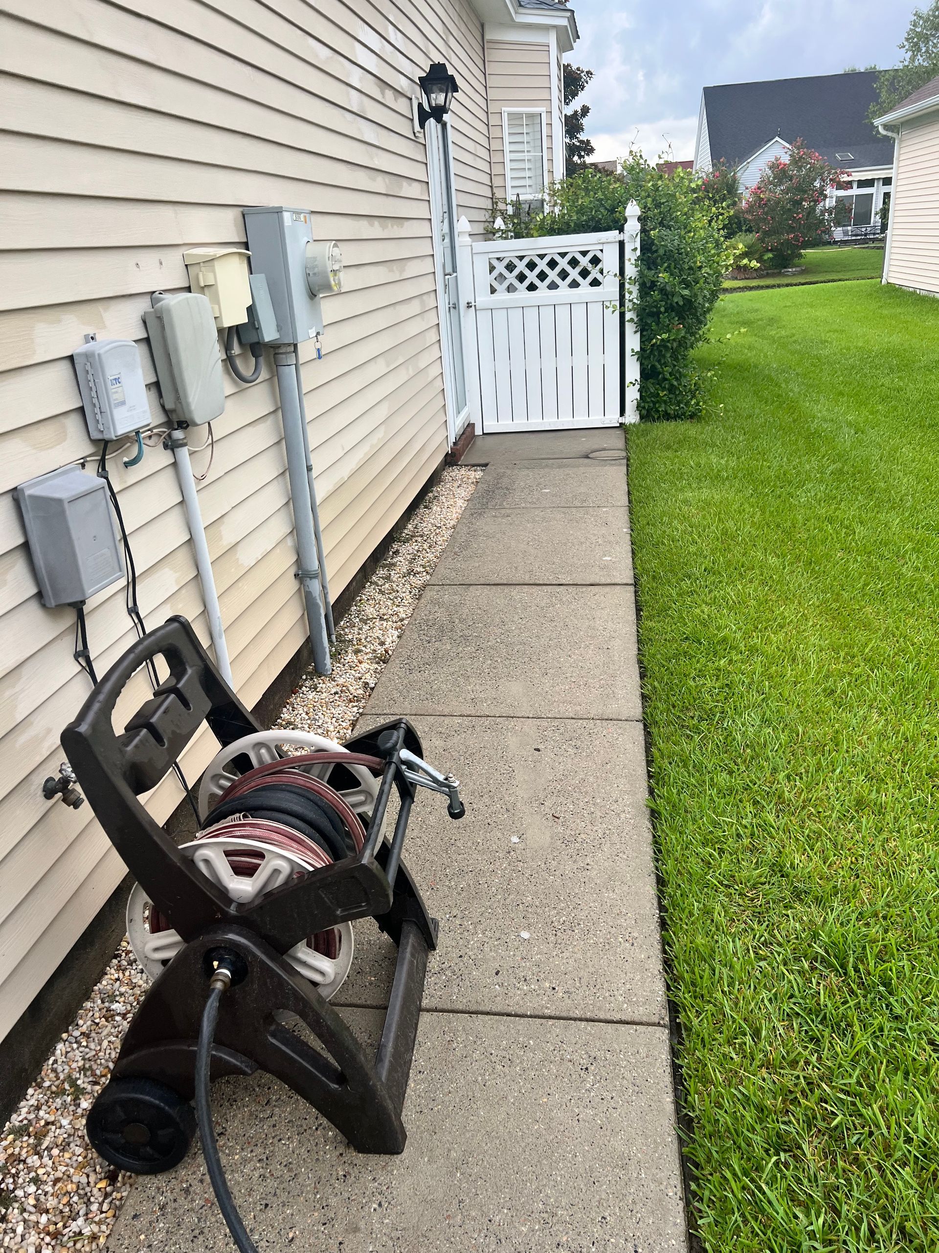 A sewer line machine sits next to a sidewalk along a house with a gate leading to a backyard.