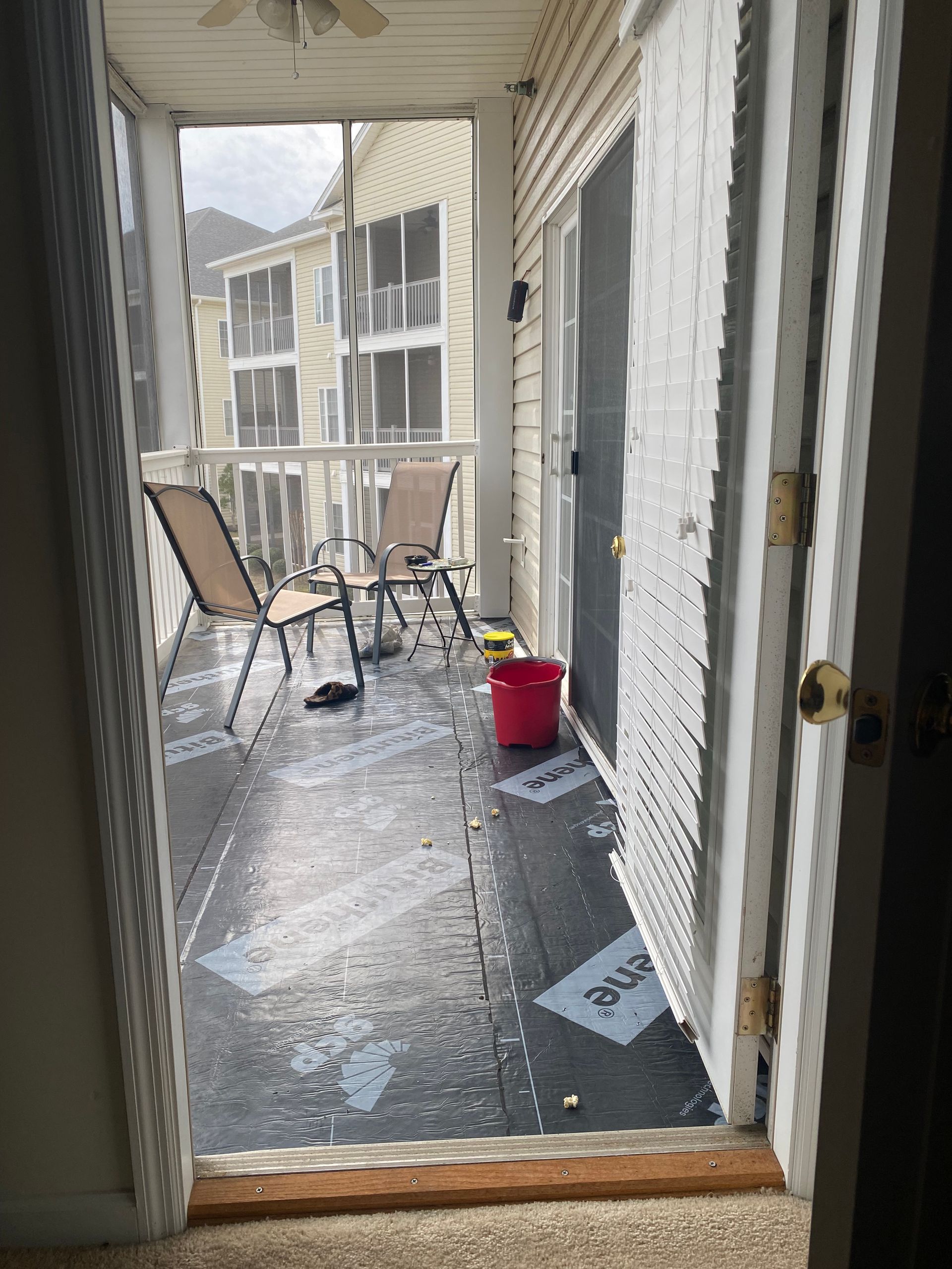 Balcony with wet floor, two chairs, and open sliding door, view from interior doorway.