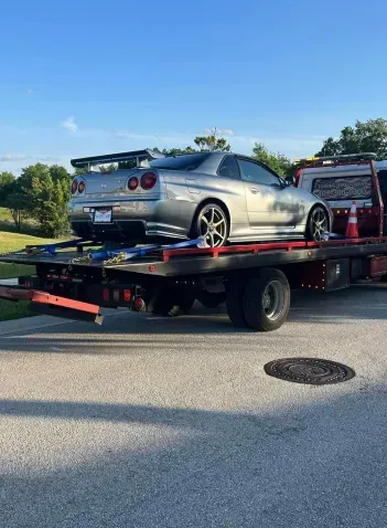 A silver sports car is being towed by a tow truck.