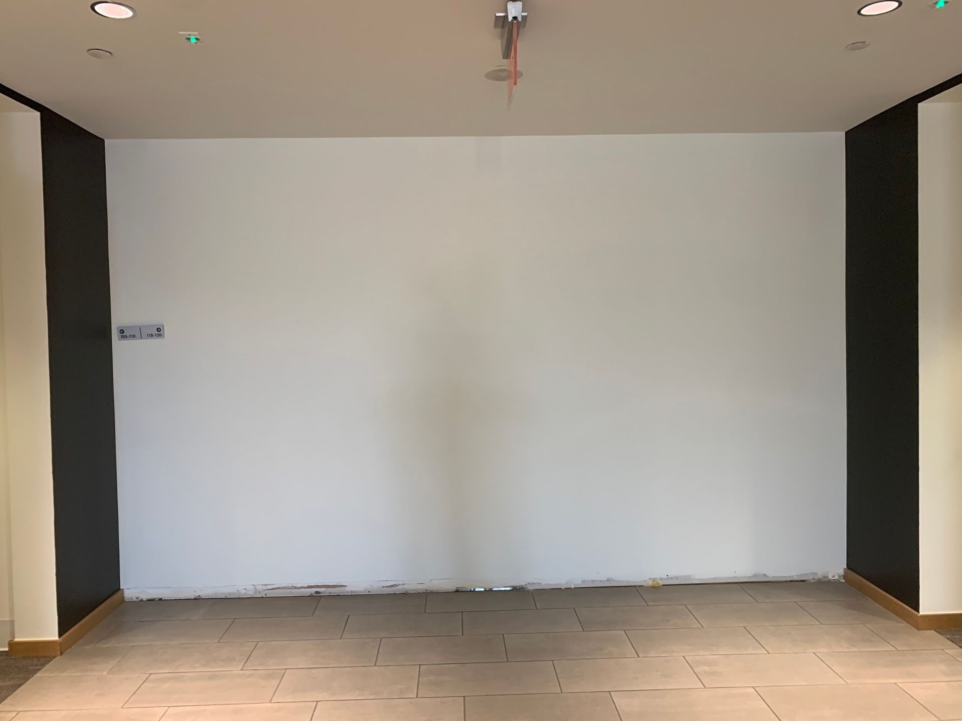 Empty white wall flanked by dark gray columns; beige floor and ceiling lights.