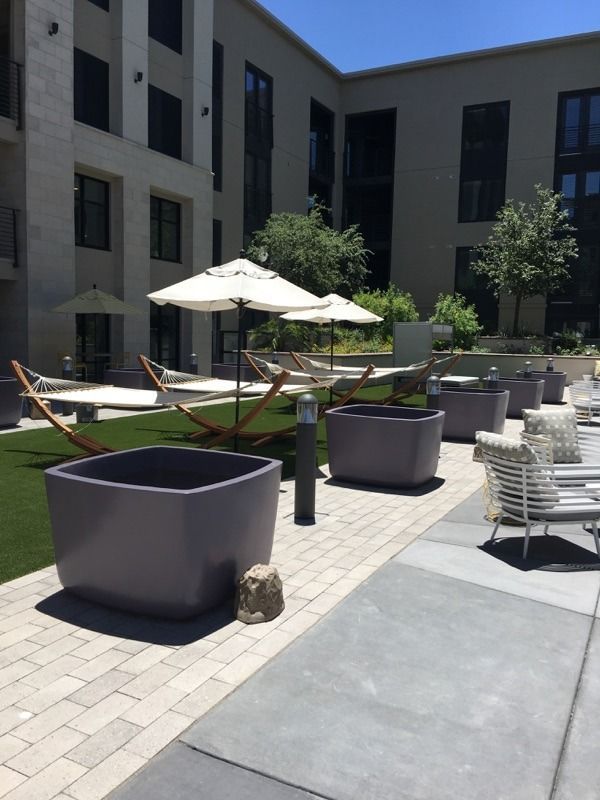Courtyard with hammocks, planters, and seating. Beige buildings in the background under a sunny sky.