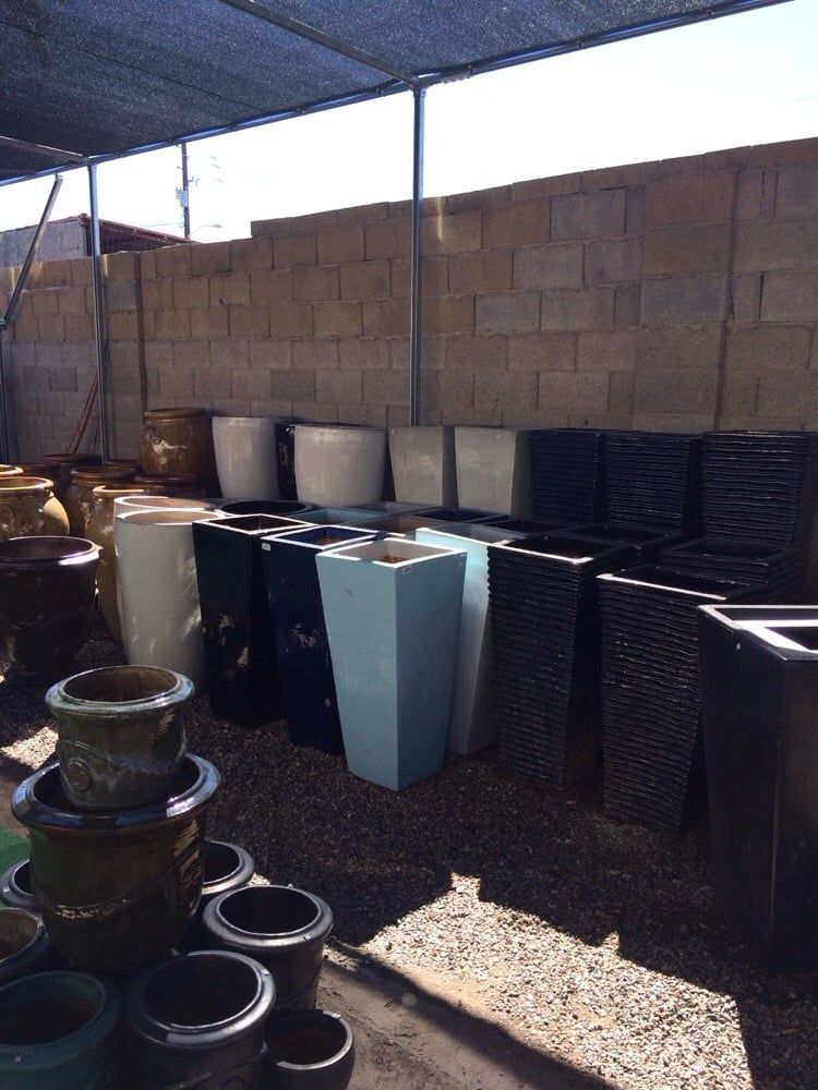 Various plant pots of different colors and shapes arranged in rows under a shaded structure.