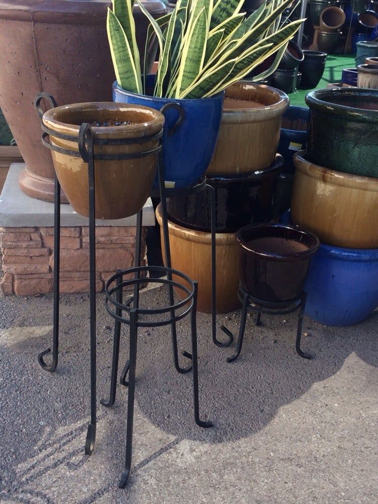 Various ceramic pots in tan, blue, and green on metal stands outdoors with a brick background.