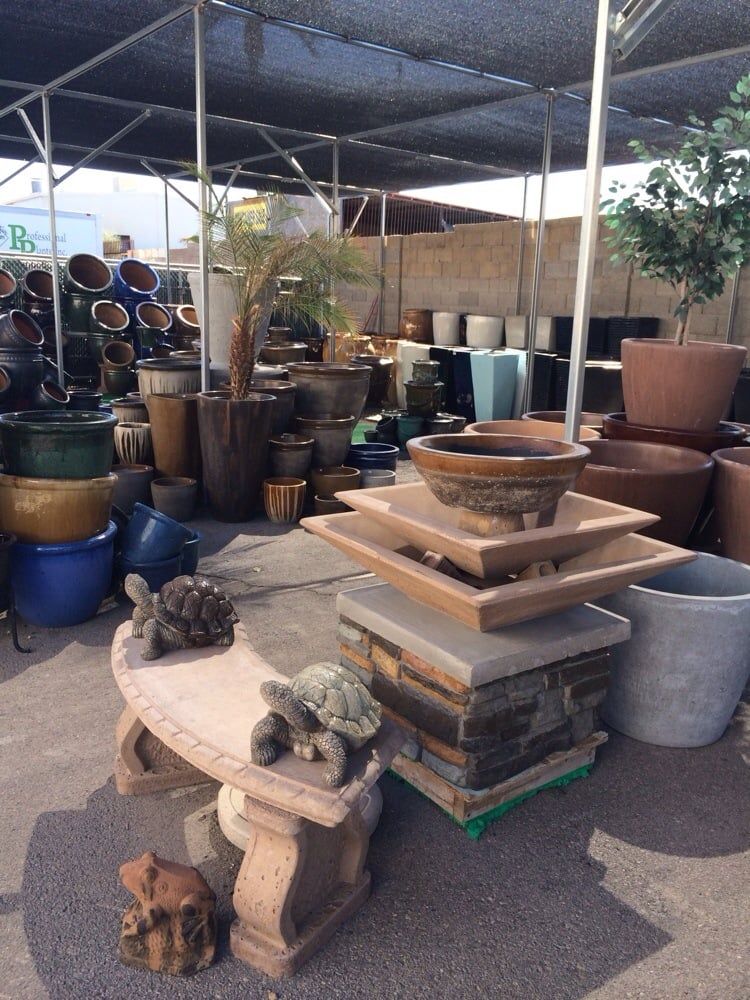 A garden center with a variety of pots, fountains, and a bench with turtle statues under a shade cloth.