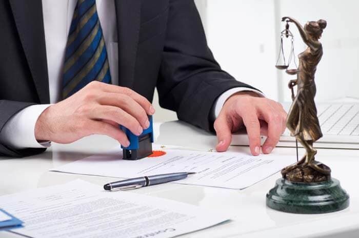 Un hombre está sellando un documento al lado de una estatua de la justicia.