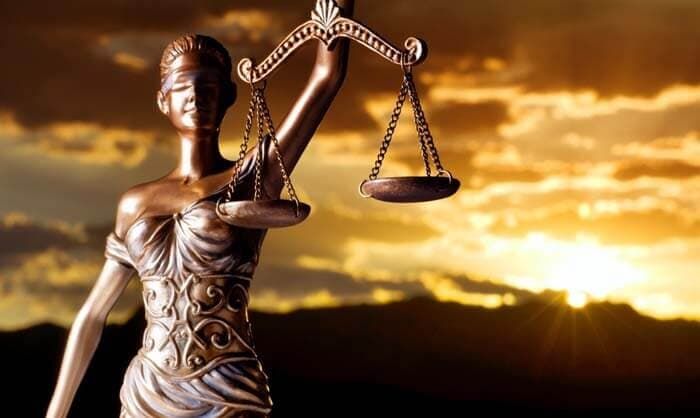 Una estatua de una mujer sosteniendo una balanza de la justicia frente a una puesta de sol.