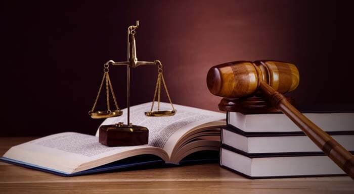 Un mazo de juez, una balanza de la justicia y una pila de libros sobre una mesa de madera.