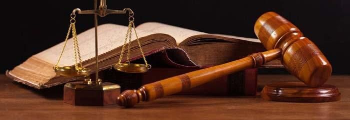 Un mazo de juez, una balanza de la justicia y un libro están sobre una mesa de madera.