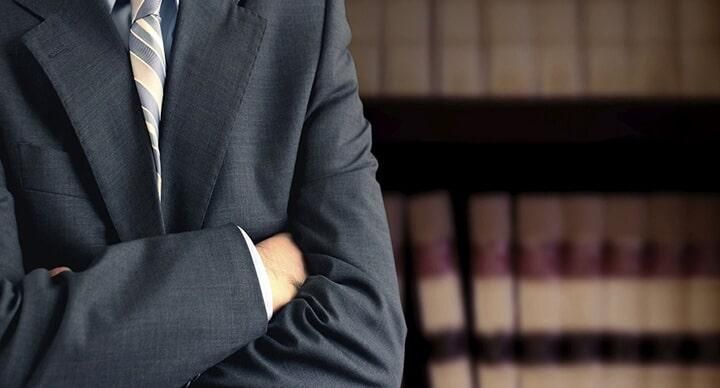 Un hombre con traje y corbata está de pie con los brazos cruzados.