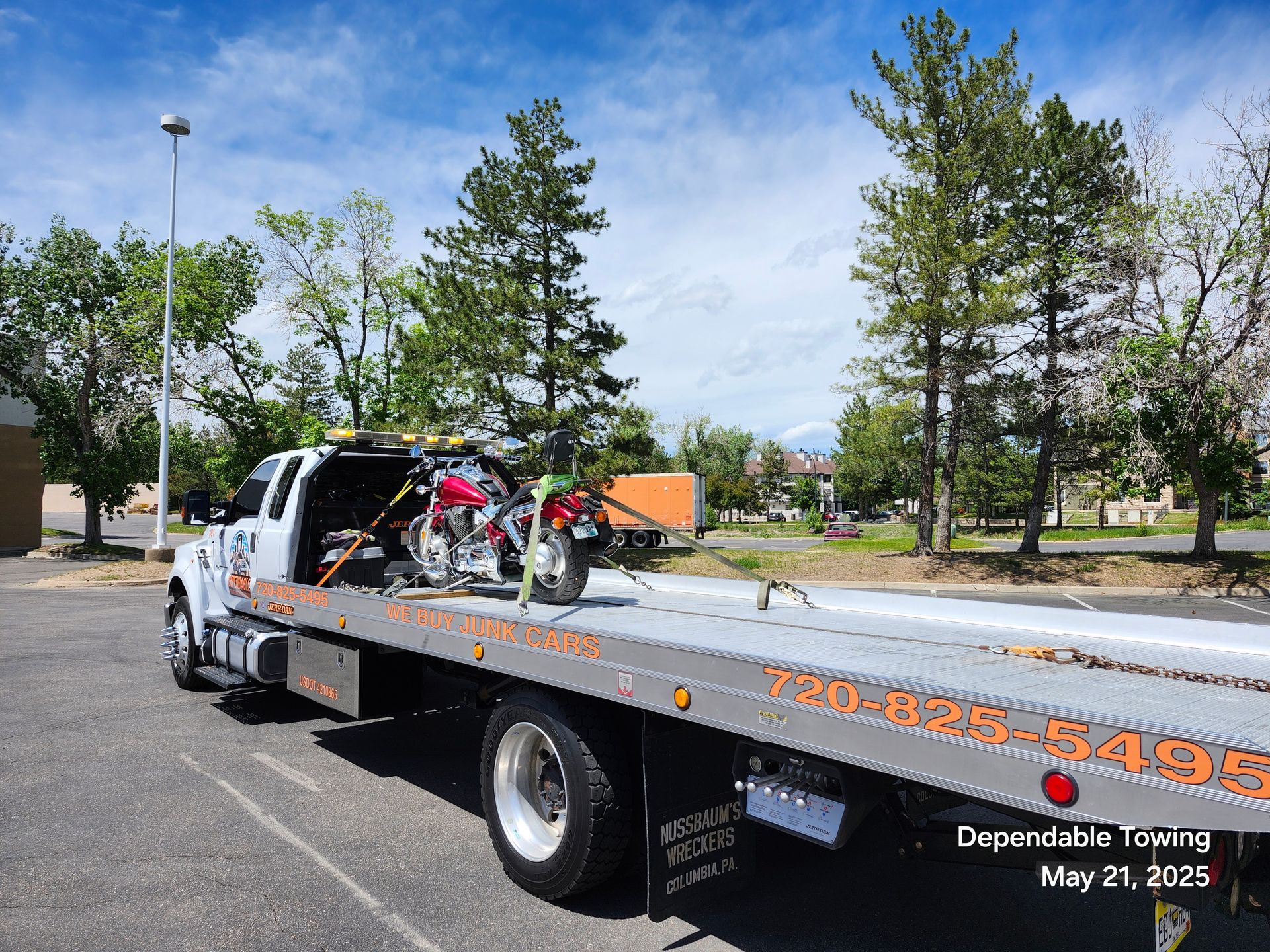 A flatbed tow truck carrying a red motorcycle parked in an outdoor lot on a sunny day.