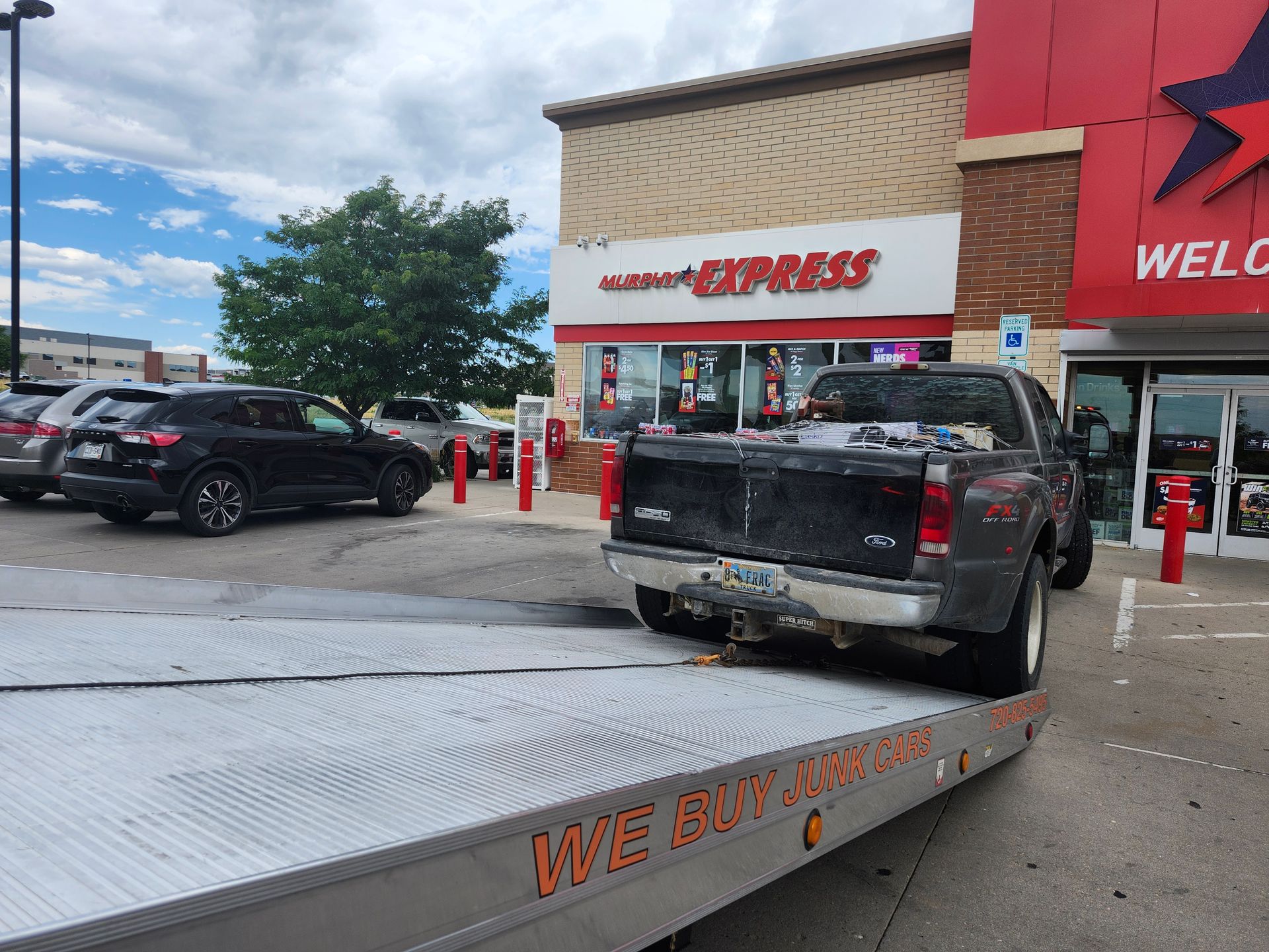 A gray pickup truck is being loaded onto a flatbed tow truck in front of a store with a large red facade.