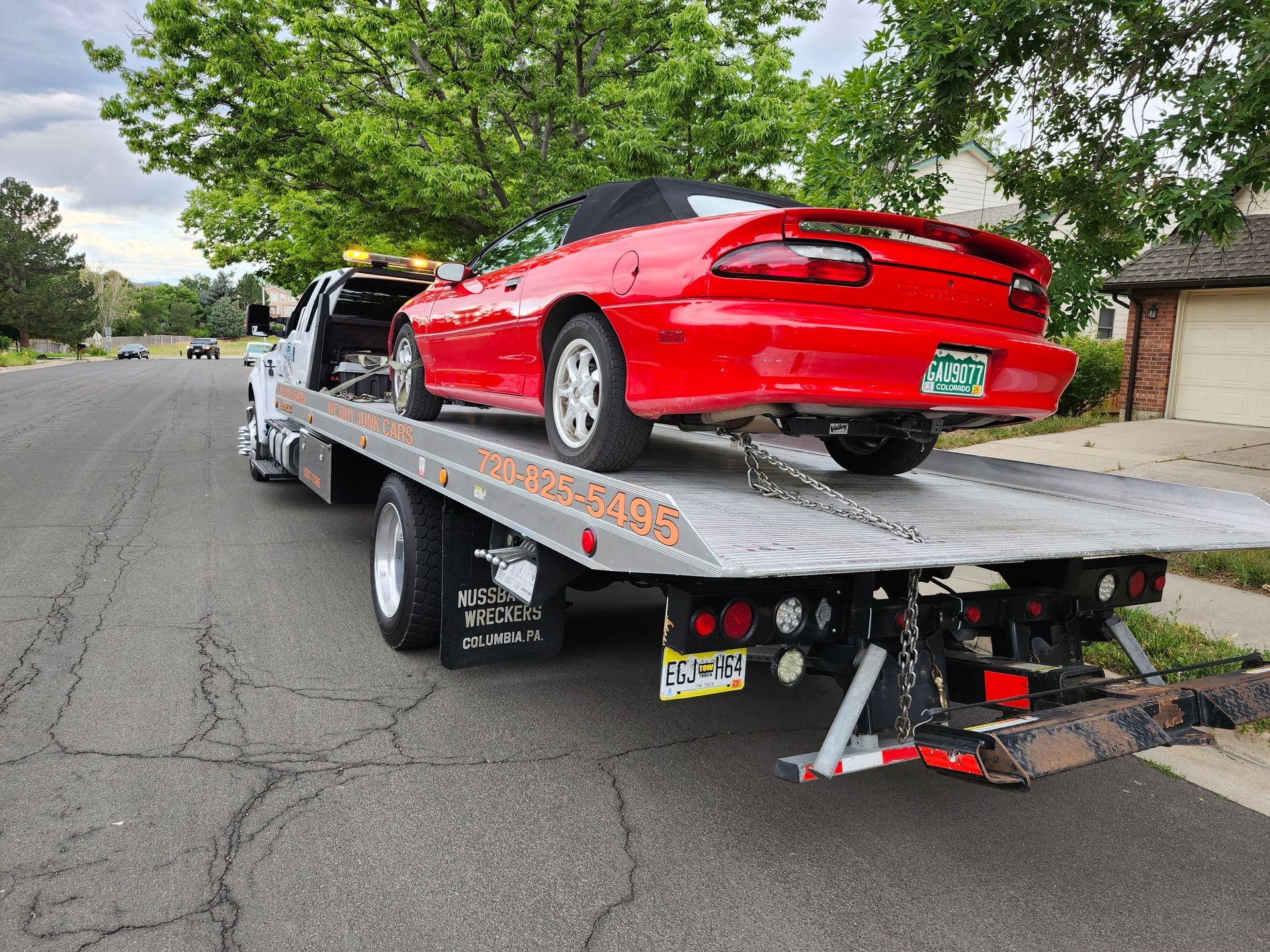 A bright red convertible sports car is secured onto the flatbed of a tow truck parked on a suburban residential street.