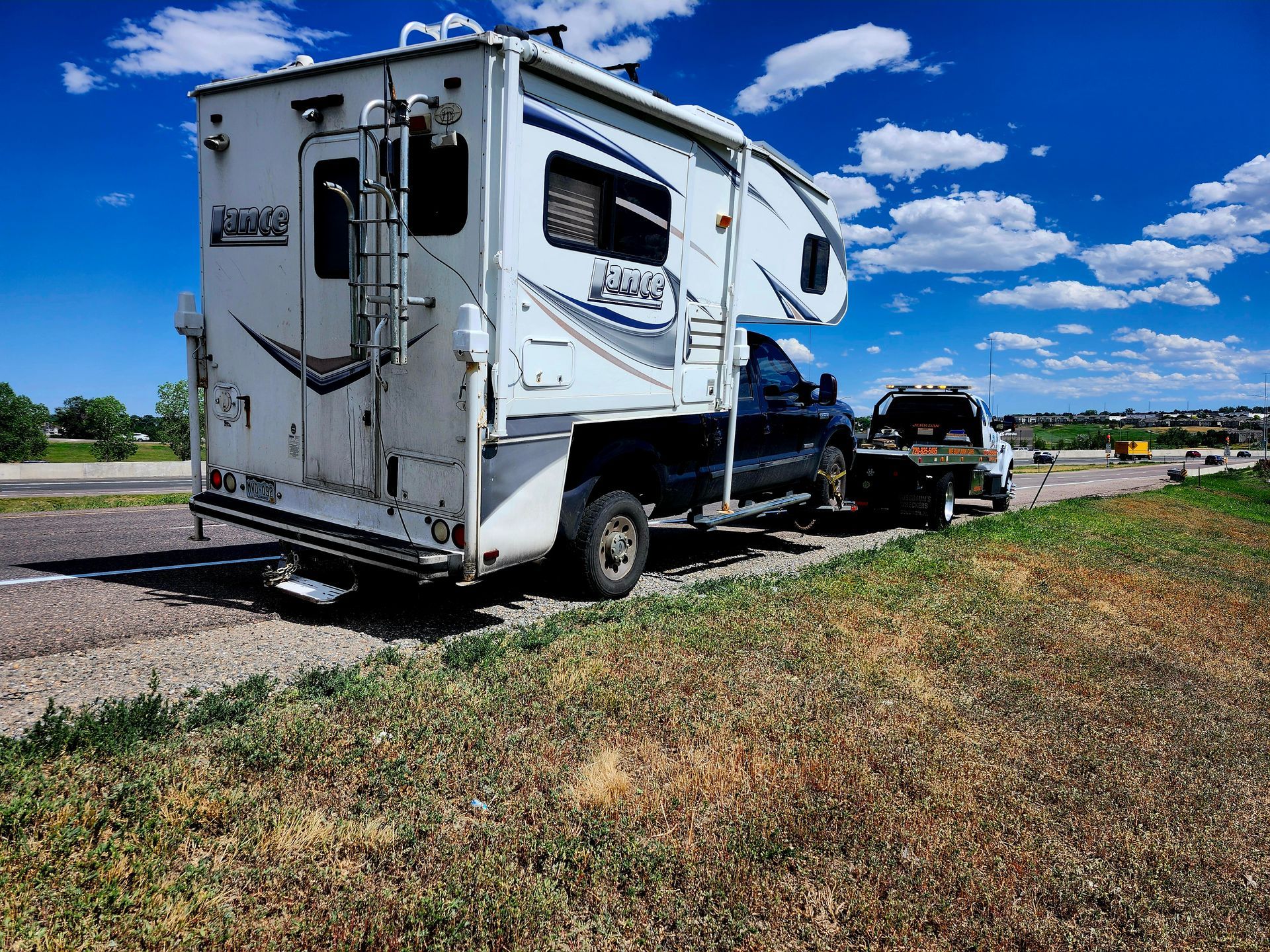 A white truck camper parked on the side of a road under a bright blue sky with scattered clouds.