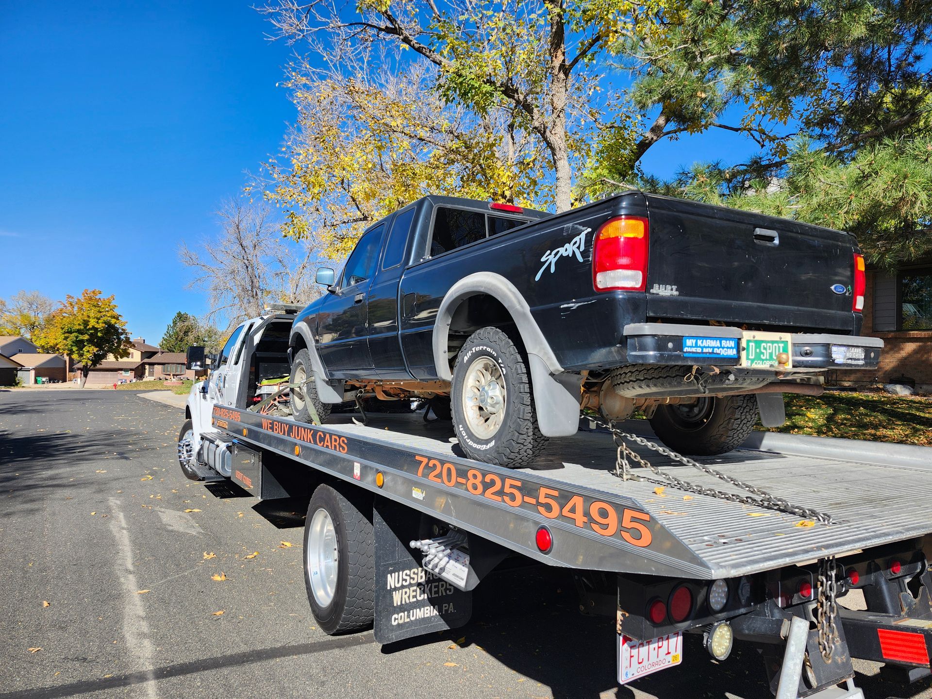 A black pickup truck being hauled on a flatbed tow truck parked on a residential street.