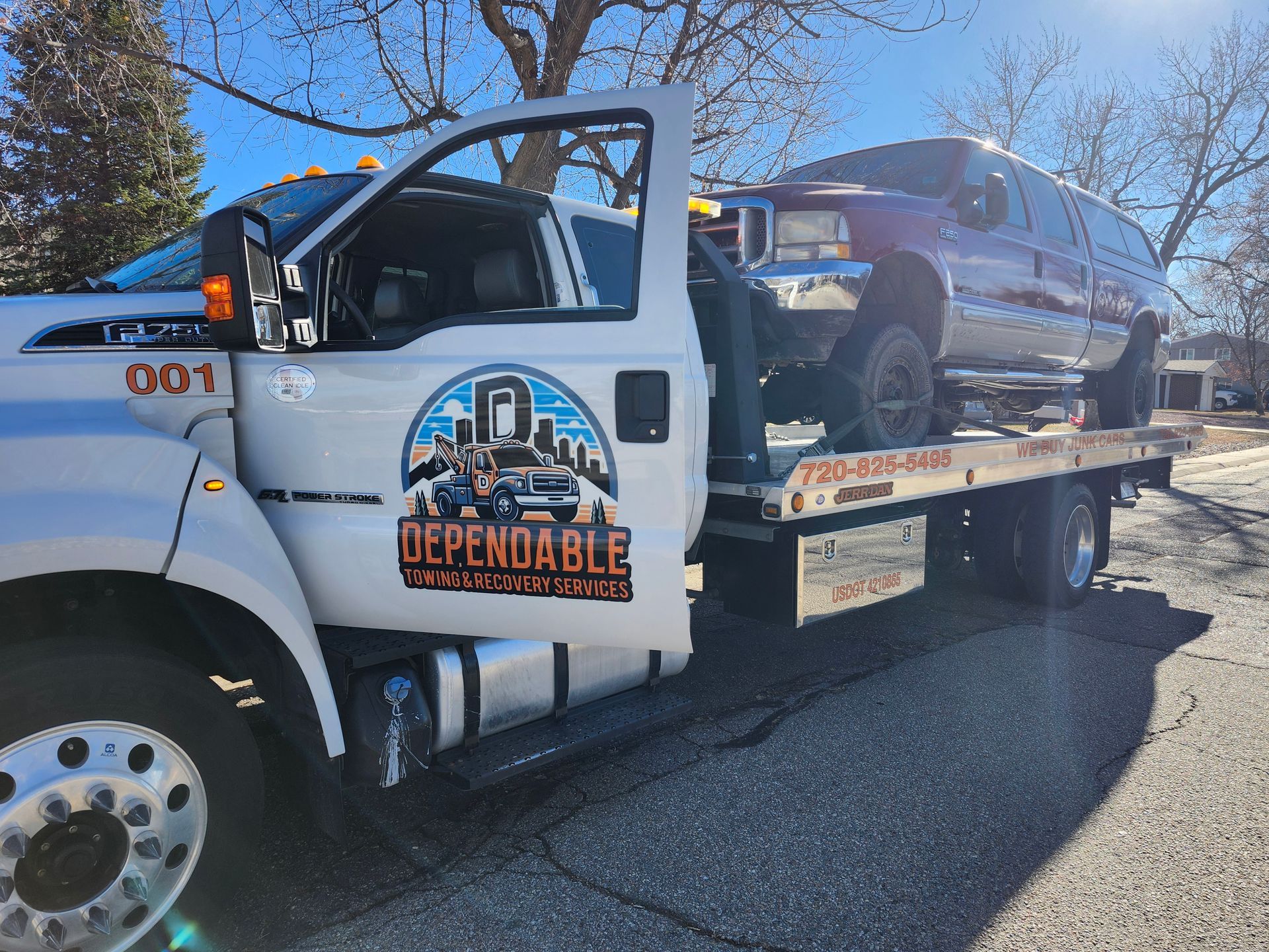 A white Dependable Towing flatbed truck hauling a maroon SUV on a sunny, residential street.