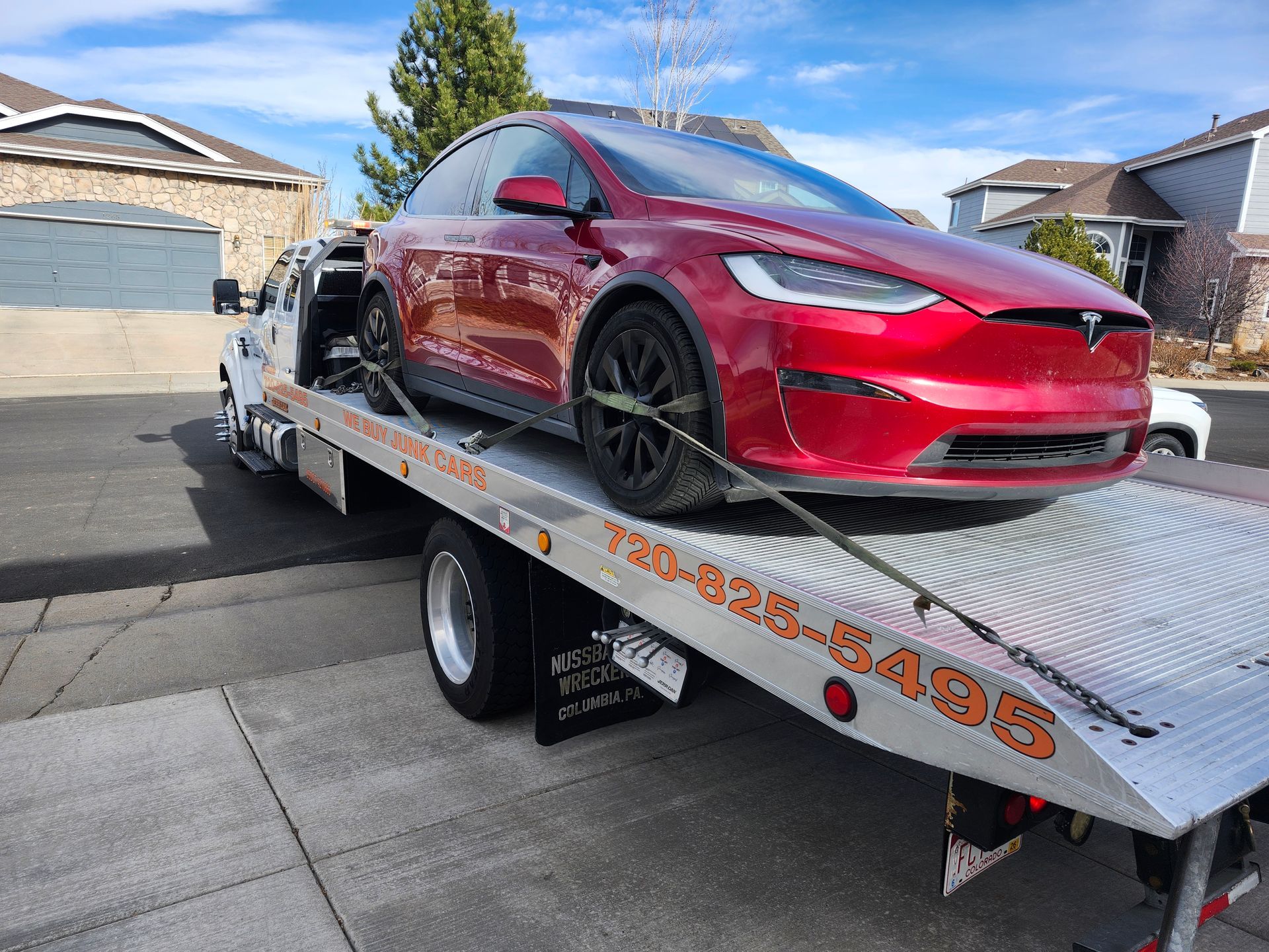 A red Tesla Model X secured on a flatbed tow truck parked in a suburban residential neighborhood.