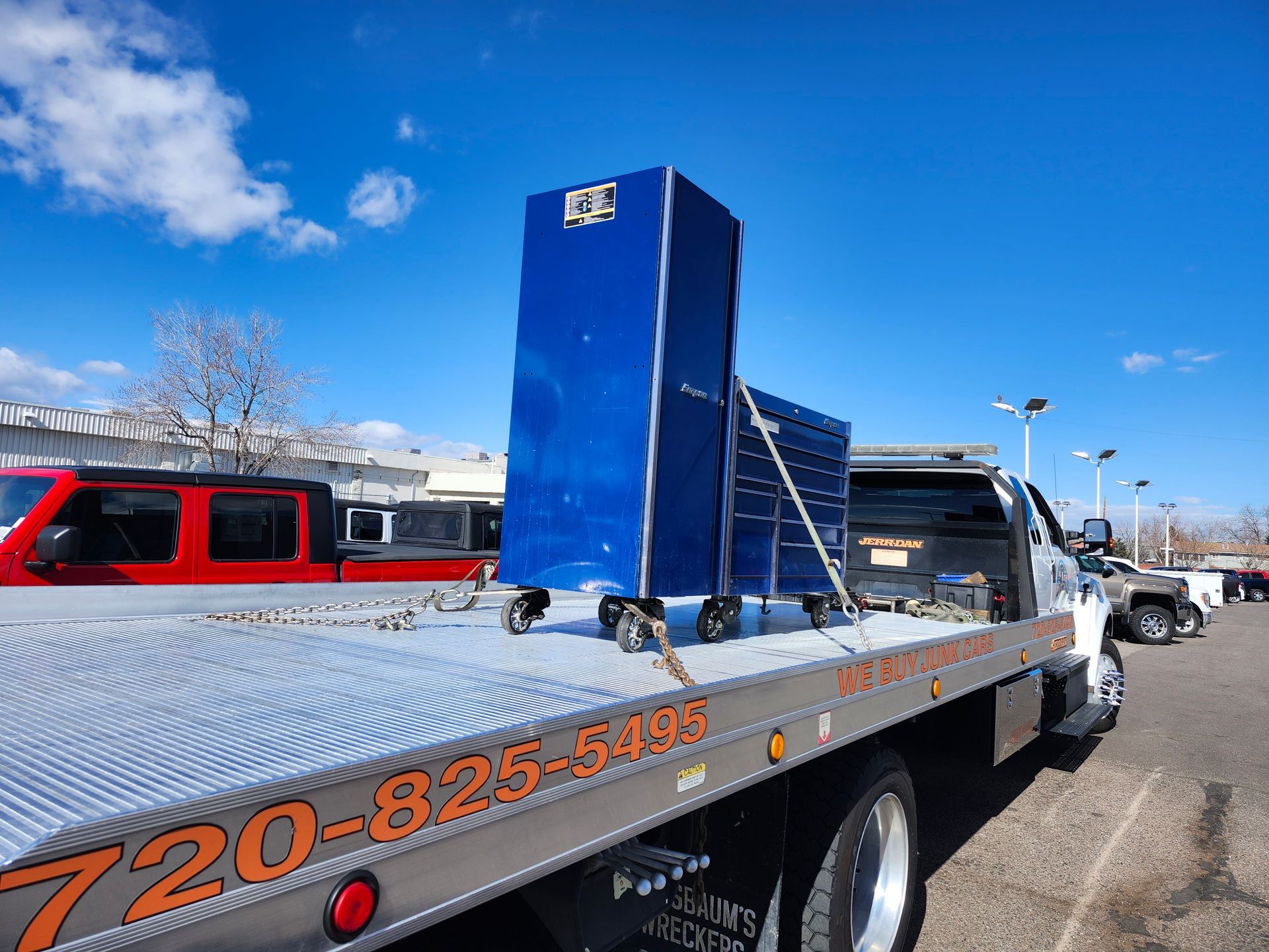 A blue metal tool cabinet secured on the flatbed of a tow truck against a bright blue sky.