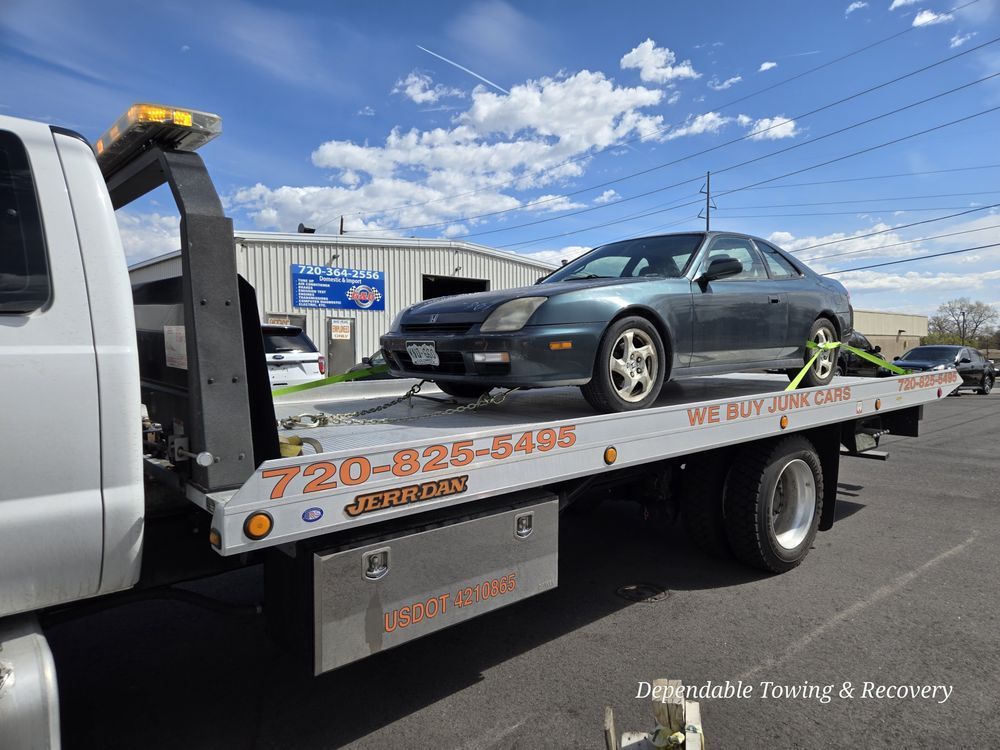 A blue sedan secured on the flatbed of a tow truck in front of a commercial building.