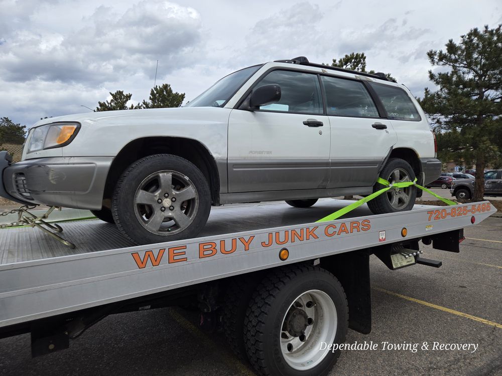 A white Subaru Forester SUV secured with green straps on a flatbed tow truck labeled 