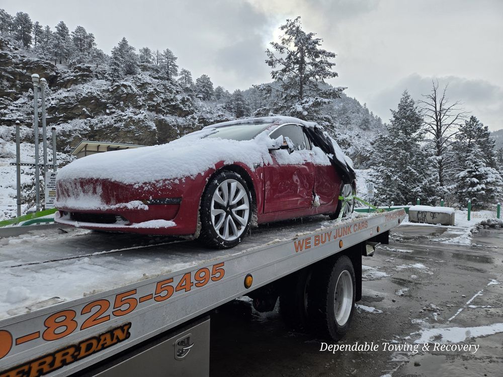A red Tesla covered in snow being transported on a flatbed tow truck in a snowy landscape.