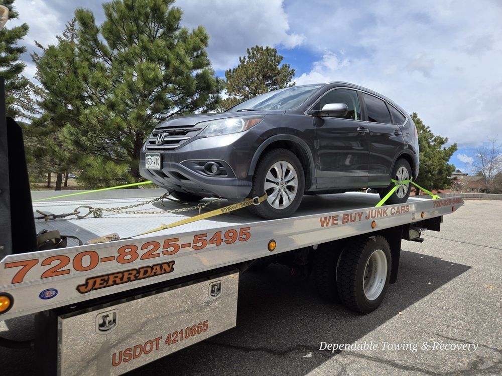A gray Honda CR-V secured with yellow tie-down straps on the flatbed of a Jerr-Dan tow truck.