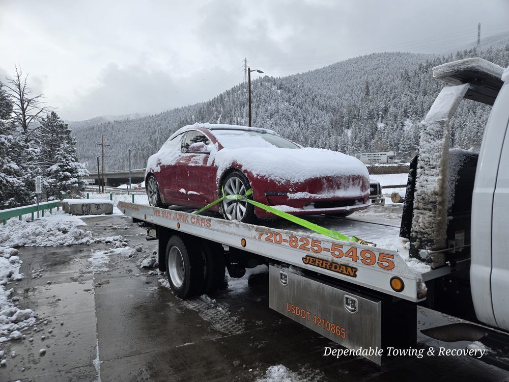 A red Tesla covered in snow being towed on a flatbed truck in a wintry, mountainous setting.