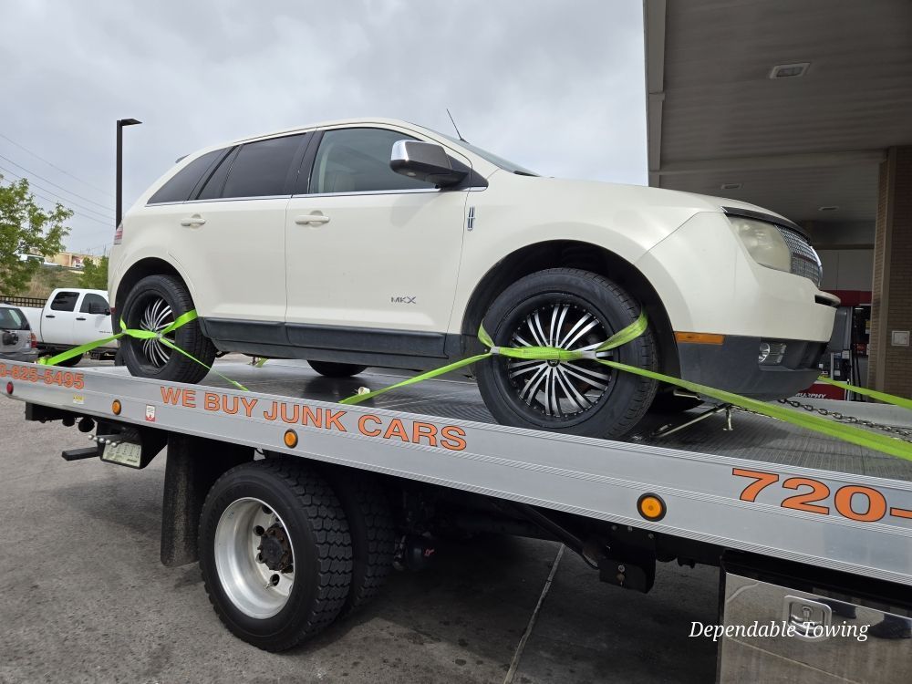 A white Lincoln SUV secured with neon green tie-down straps on the bed of a flatbed tow truck.