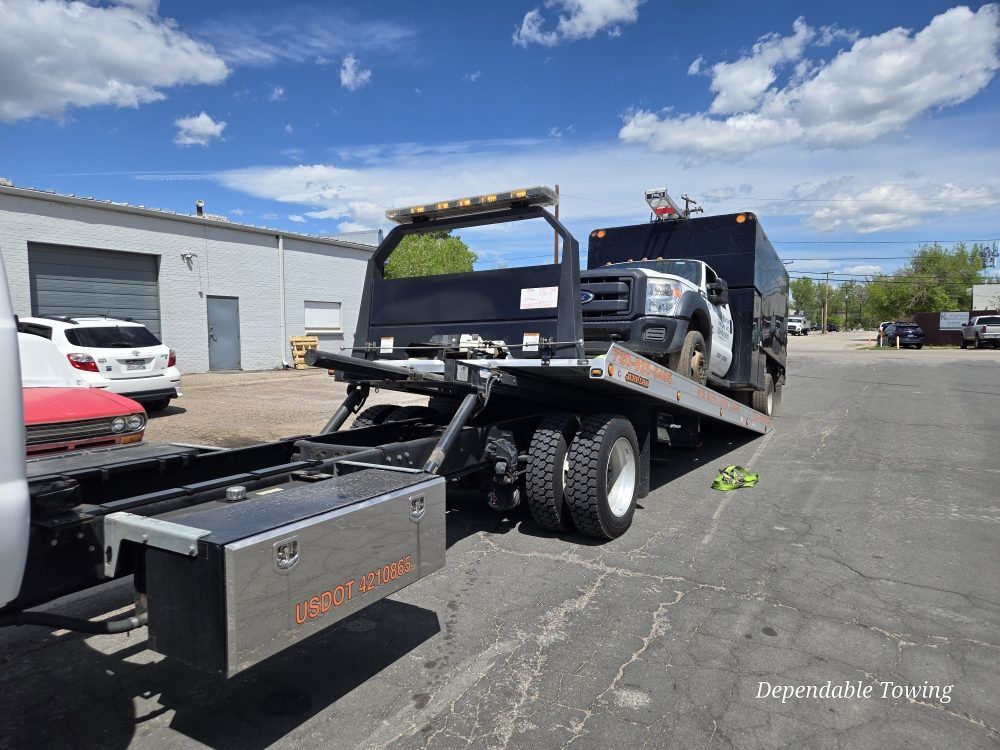 A black tow truck with a tilted flatbed platform is parked in an outdoor lot on a sunny day.