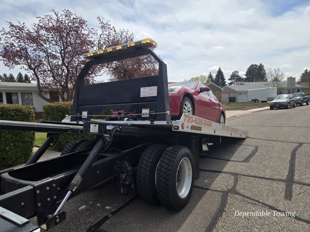 A red car secured on a flatbed tow truck parked on a sunny residential street.