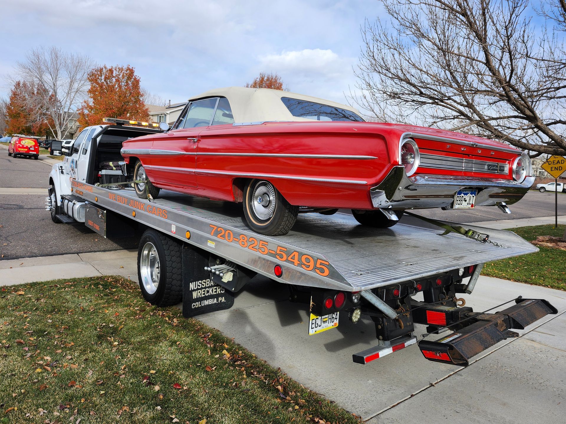 A bright red vintage convertible car with a white top being transported on the back of a flatbed tow truck.