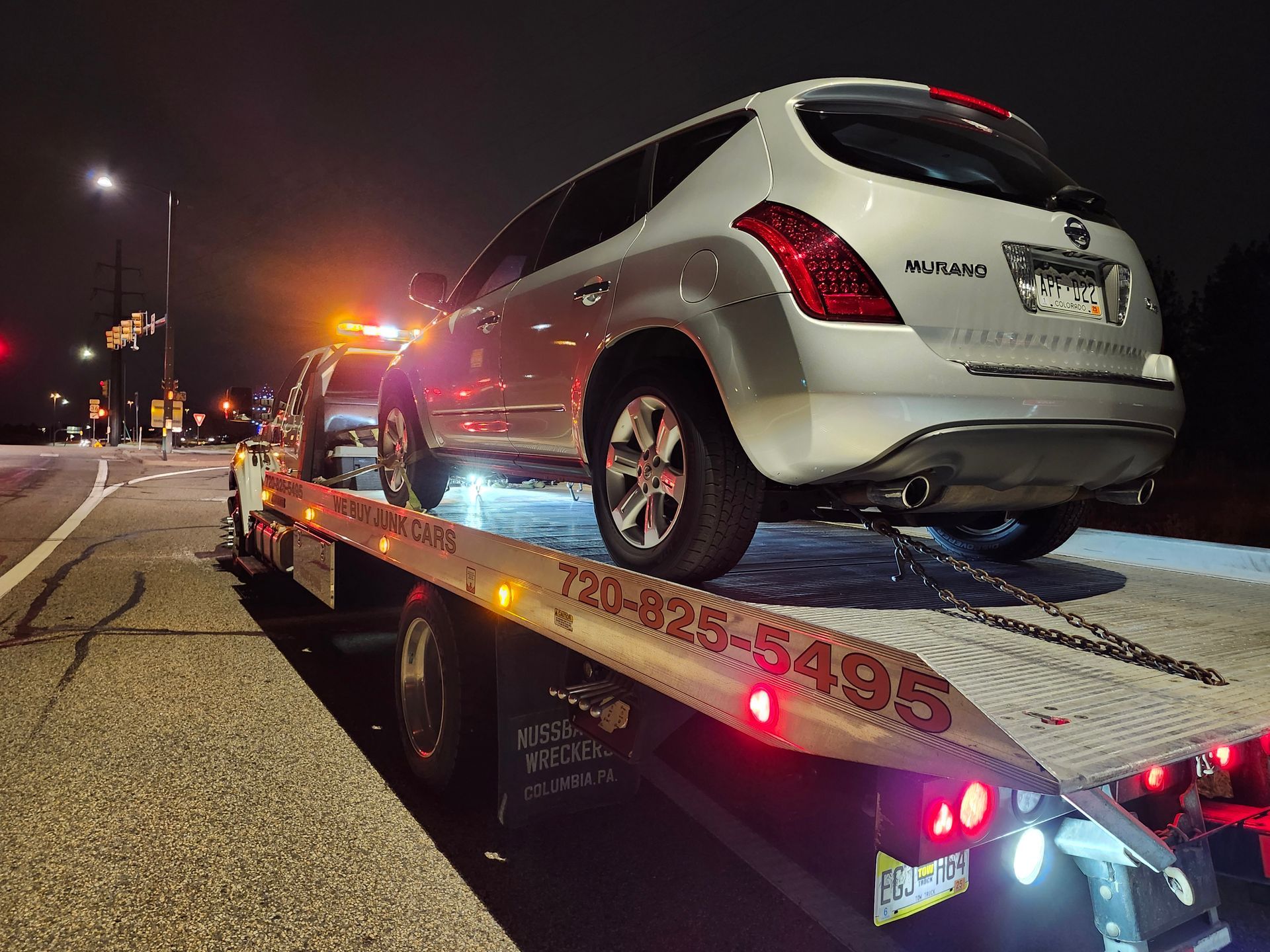 A silver Nissan Murano loaded onto a flatbed tow truck at night.