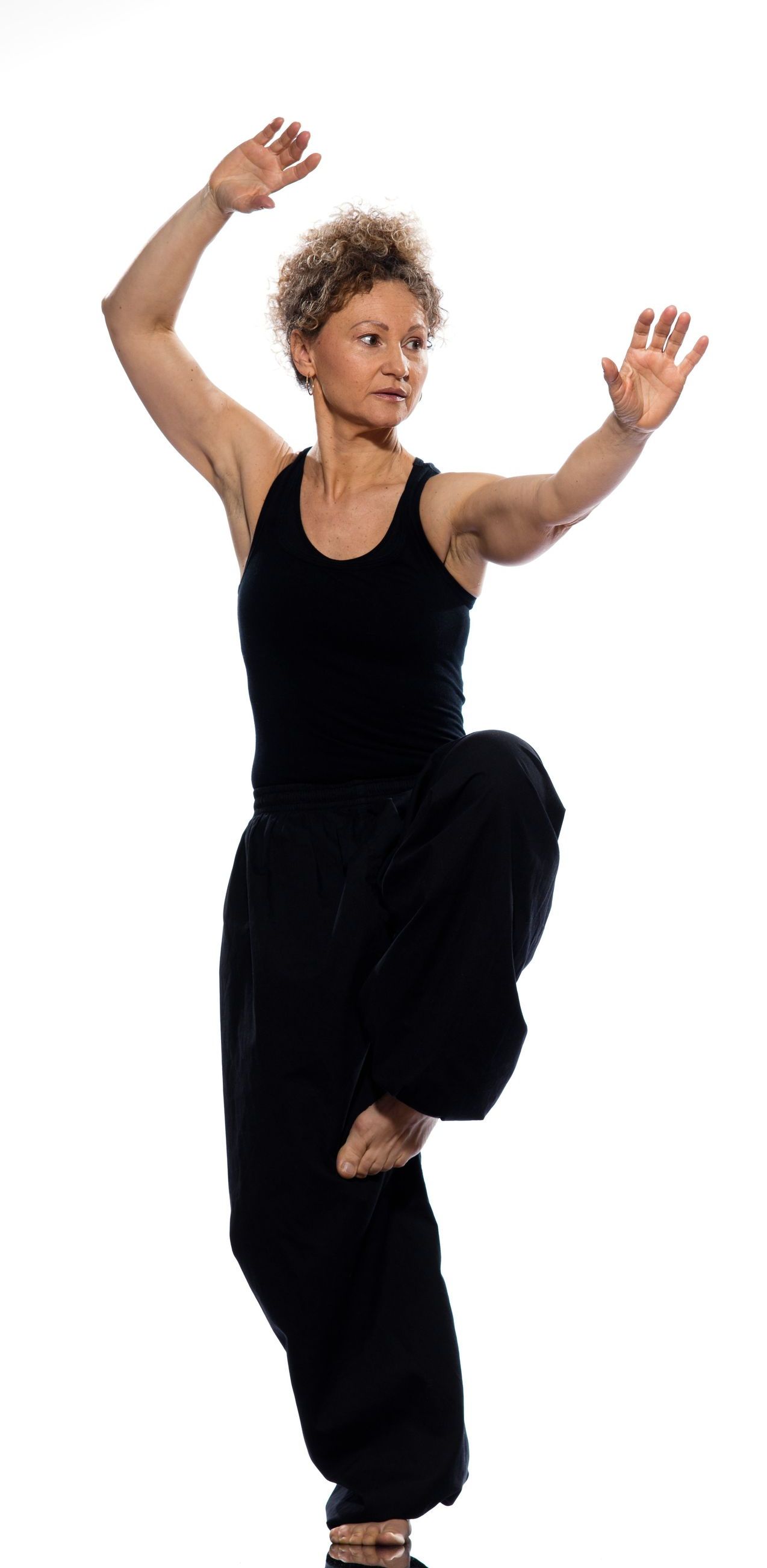 A woman in a black tank top and black pants is standing on one leg.