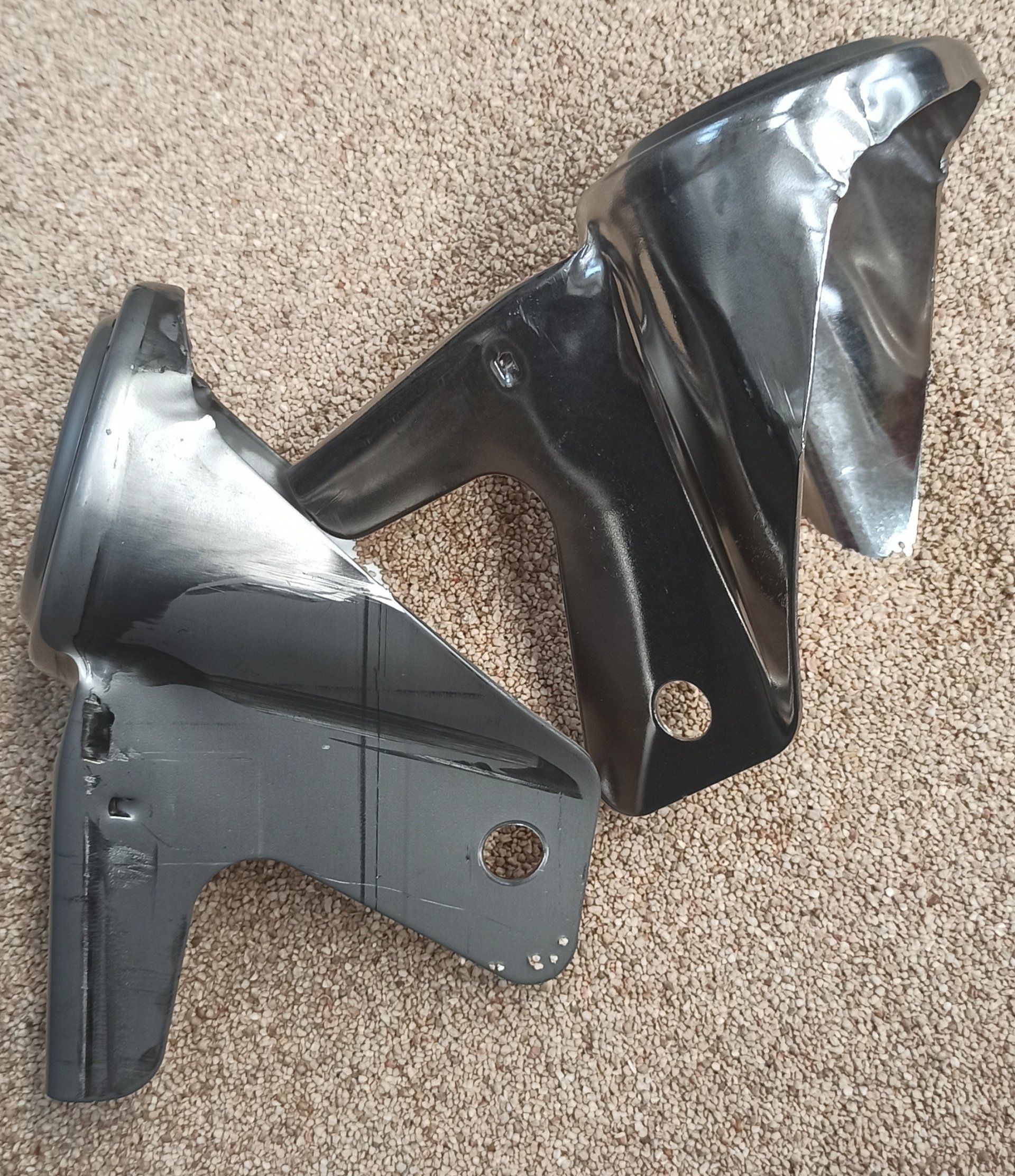 Due staffe di sospensione per auto in metallo nero su un tappeto color cuoio.