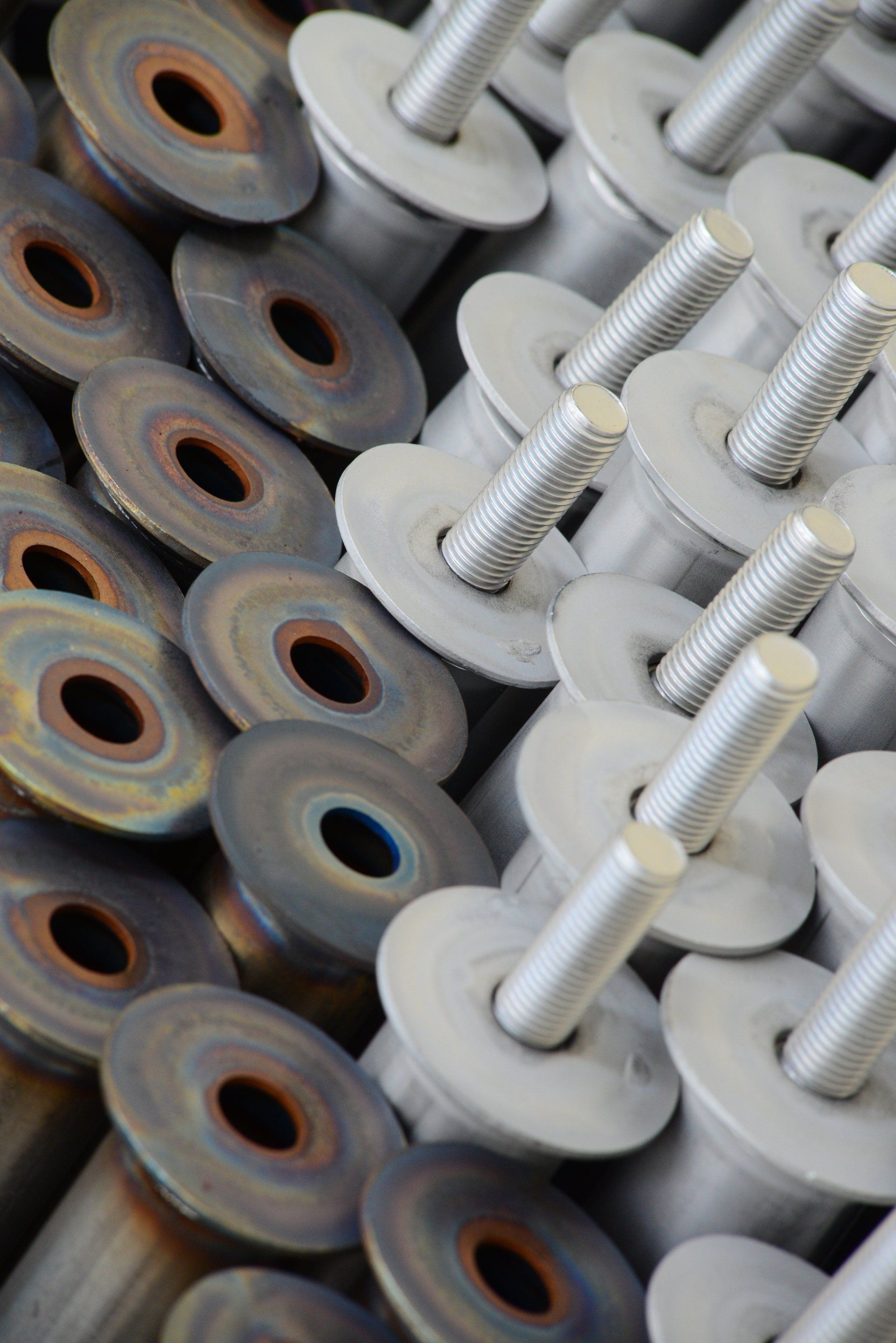 Bulloni metallici con rondelle circolari, alcuni di colore scuro, altri argentati, disposti uno vicino all'altro.