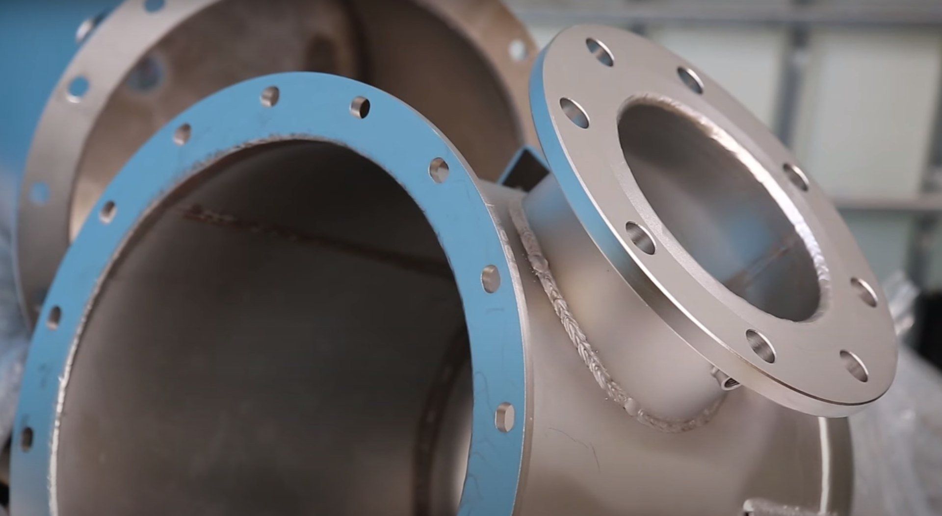 Giunto a T in acciaio inox con flange. Guarnizione blu visibile sull'apertura.