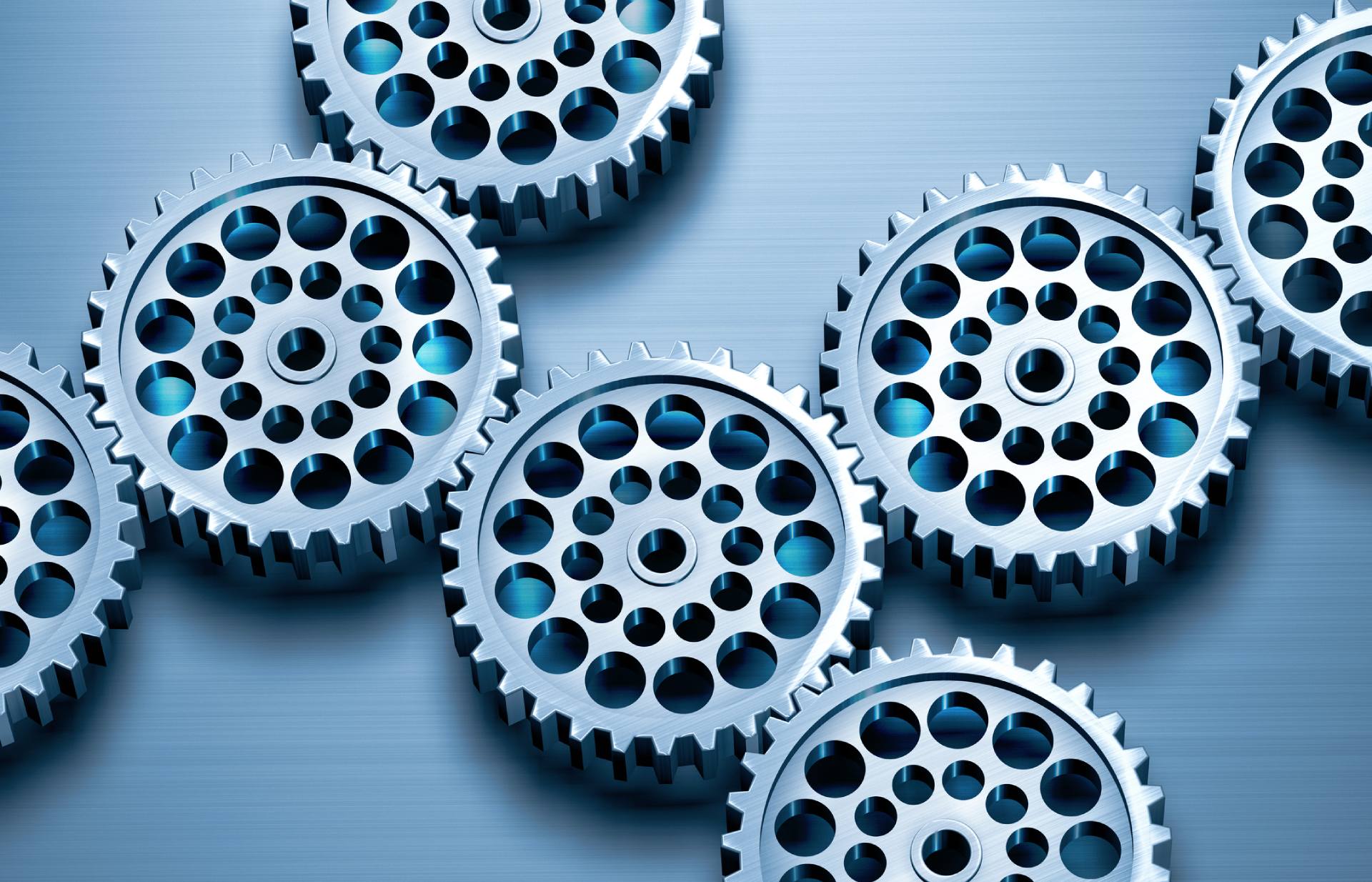 Primo piano di diversi ingranaggi metallici con più fori, sparsi su una superficie metallica spazzolata grigio-blu.