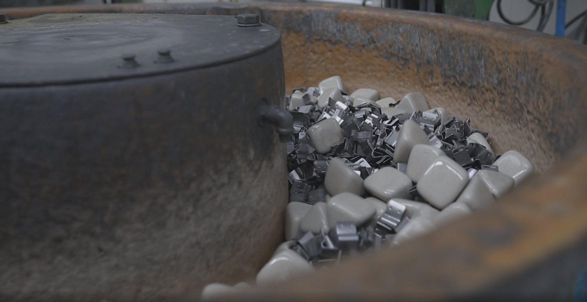 Parti metalliche e pietre che rotolano in una grande macchina industriale, probabilmente per essere lucidate.