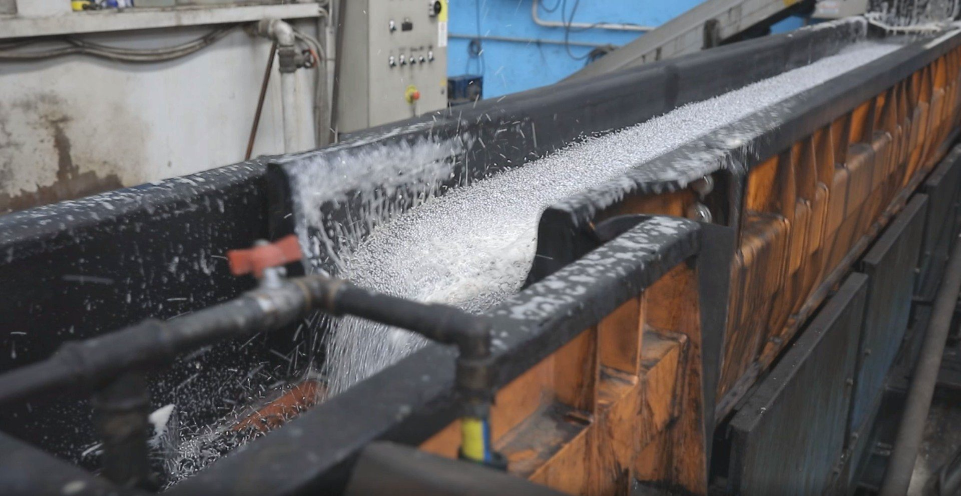 Un lungo trogolo industriale pieno di materiale metallico in movimento, probabilmente in fase di raffreddamento o lavorazione.