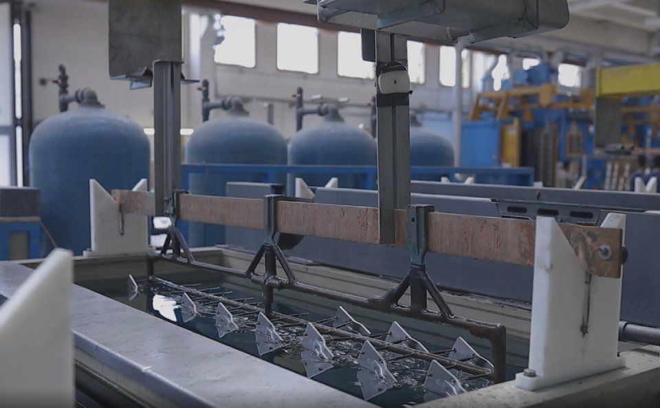 Processo industriale: parti metalliche immerse in un bagno chimico. Serbatoi blu sullo sfondo.