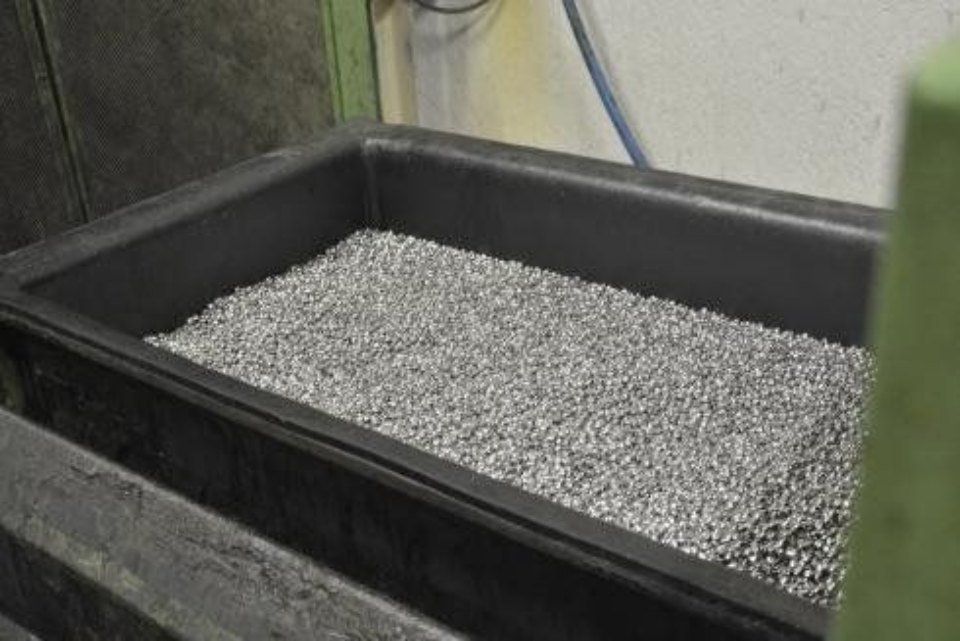 Contenitore nero pieno di piccoli pezzi di metallo argentato in una configurazione da fabbrica.