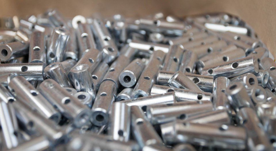 Mucchio di piccole parti metalliche cilindriche, ciascuna dotata di fori, viste da vicino.
