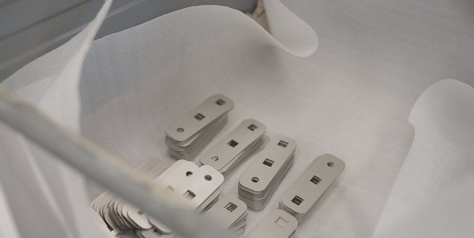 Parti rettangolari in metallo impilate in un contenitore bianco rivestito di carta.