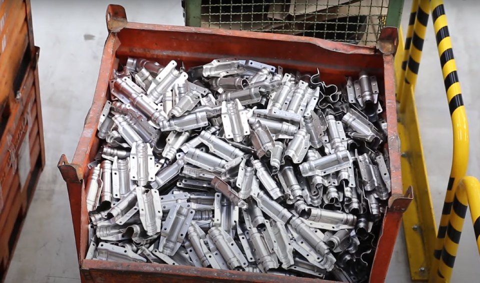 Parti metalliche in un bidone arancione, probabilmente in una fabbrica.