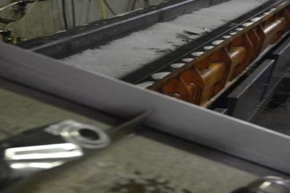 Un trasportatore meccanico con liquido schiumoso, che lavora oggetti lunghi e di colore chiaro.