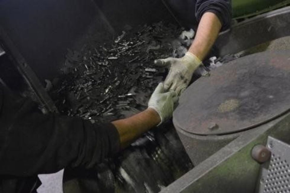 Due operai con i guanti selezionano rottami metallici vicino ai macchinari.