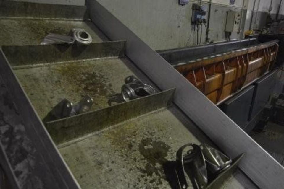 Parti metalliche in un vassoio industriale sporco, accanto a un contenitore più grande arancione e marrone.