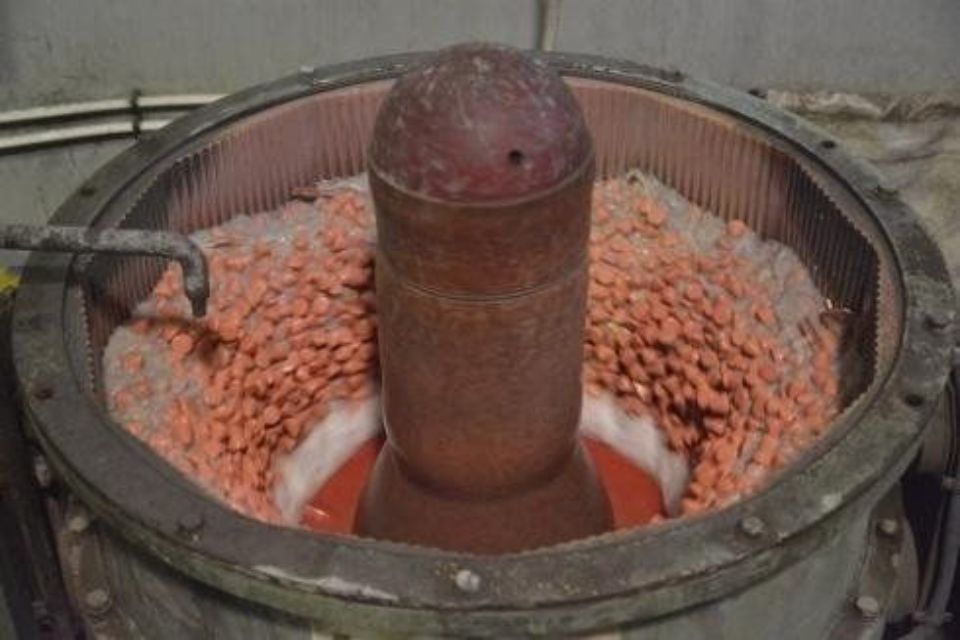 Macchina industriale che lavora oggetti color rame, possibilmente per lucidarli o rifinirli.