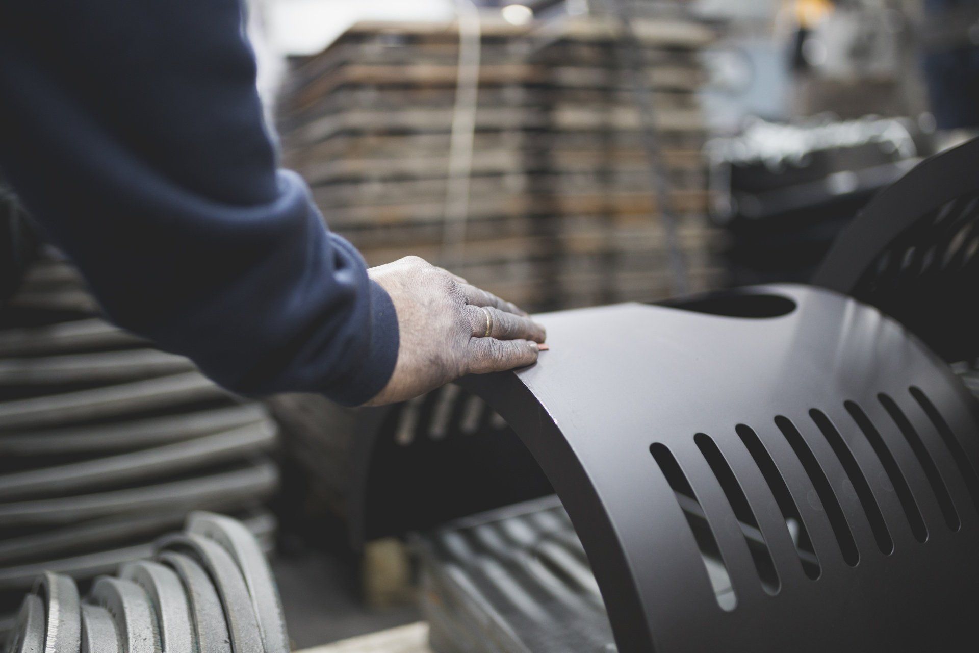 Mano di una persona che tocca un oggetto metallico nero curvo con aperture scanalate in una configurazione di fabbrica.