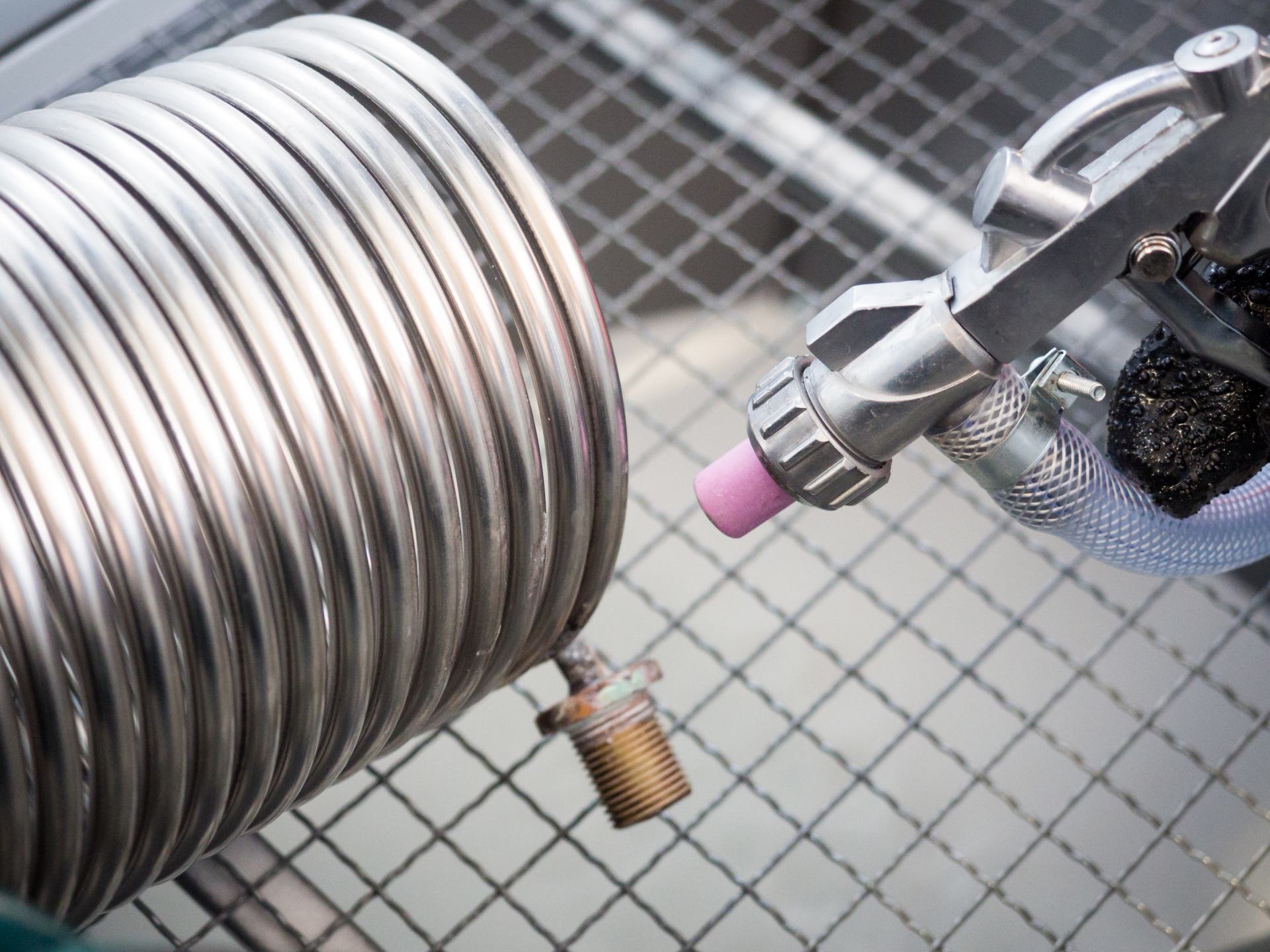 Una persona utilizza una sabbiatrice per pulire un tubo metallico arrotolato all'interno di una rete metallica.